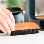 Hand, die mit einer Holzbürste Kaffeesatz von einer Arbeitsplatte wischt.